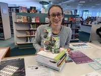 This is an image of library staff member Andi Hirsh next to a pile of books and canned food.