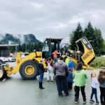 This picture was taken during Day of Play last year. It shows several kids and parents lined up to get on a piece of heavy machinery.