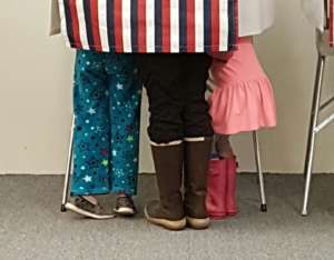 This is a picture of a voting booth with what's clearly the legs of three children showing underneath.