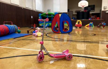 IMG_1919 A pink scooter stands unoccupied with other toys and the bouncy house in the background during Preschool Open Gym.