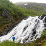 This is a picture of a beautiful Juneau waterfall and a person looking at it.