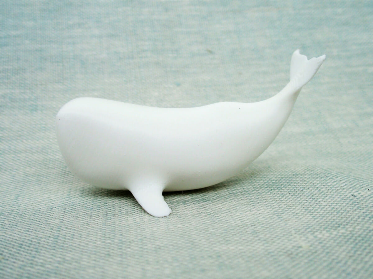 A model of a sperm whale, printed in white Tough PLA. The form is simplified and abstracted, and the whale's tail curves up above its back.