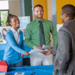 This image shows two job seekers interacting with an employer at a job fair.