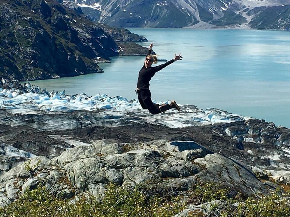 Walk Southeast 2022 participant jumping on a rock with the glacier and lake behind them.