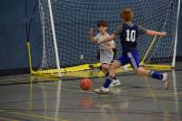 Photo of two small children chasing a soccer ball in a gym.
