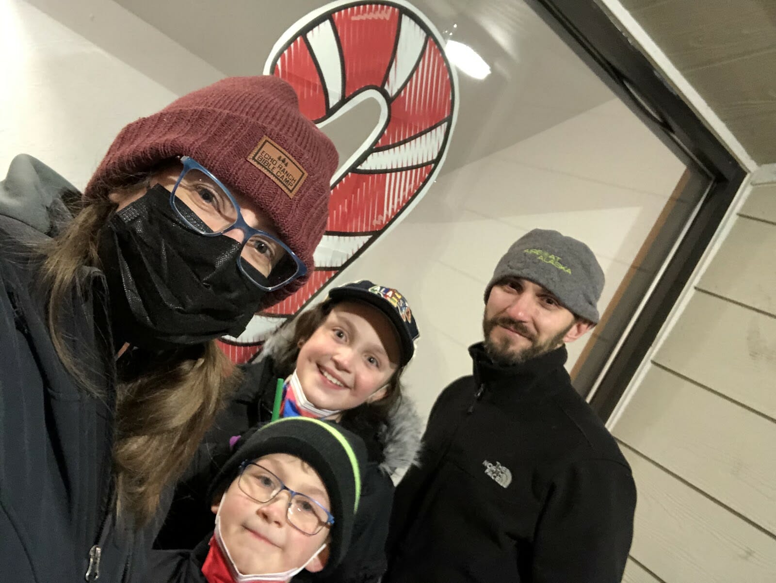 A family selfie in front of a giant candy cane in the window.