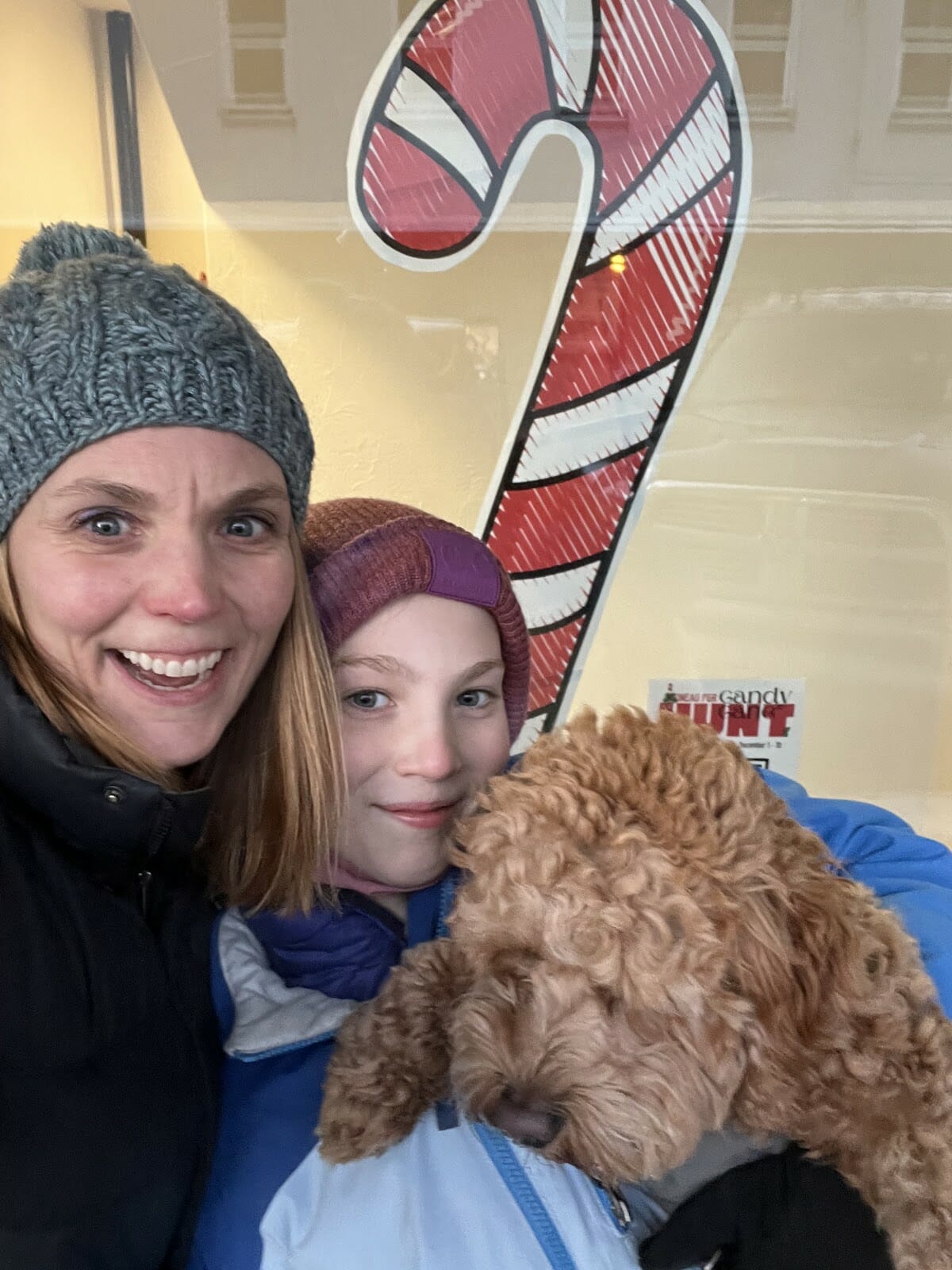 A woman, young girl and curly-haird puppy in front of a candy cane.