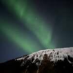 Photo of green aurora above snowy mountain