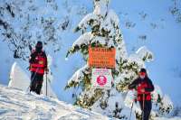Photo of two ski patrol members and an Avalanche Warning sign