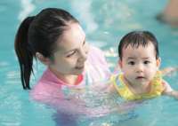 Photo of adult woman supporting infant in the pool.