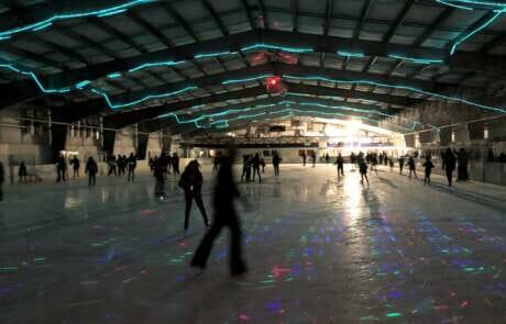 Photo of people skating at Treadwell Arena ice rink lit with rainbow lights