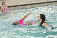 Photo of swim instructor in pool supporting child learning backstroke