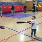Photo of small child swinging wiffle bat in gymnasium