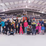 Photo of children and adult skaters posing in front of Zamboni on Treadwell Arena ice rink