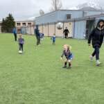 Photo of small children and adult instructor playing with soccerball outdoors