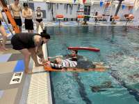 Photo of lifeguarding students watching instructor demonstrate lifesaving techniques in pool