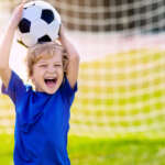 Photo of small child standing in front of soccer net holding soccer ball