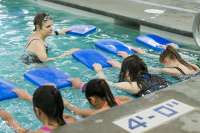 Photo of swim instructor in the pool speaking to several young swimmers with kickboards