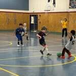 Photo of several children playing indoor soccer in a gym.