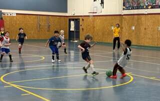 Photo of several children playing indoor soccer in a gym.
