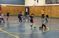 Photo of several children playing indoor soccer in a gym.