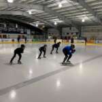 Photo of instructor leading several students in speed skating exercise on indoor ice