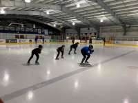 Photo of instructor leading several students in speed skating exercise on indoor ice