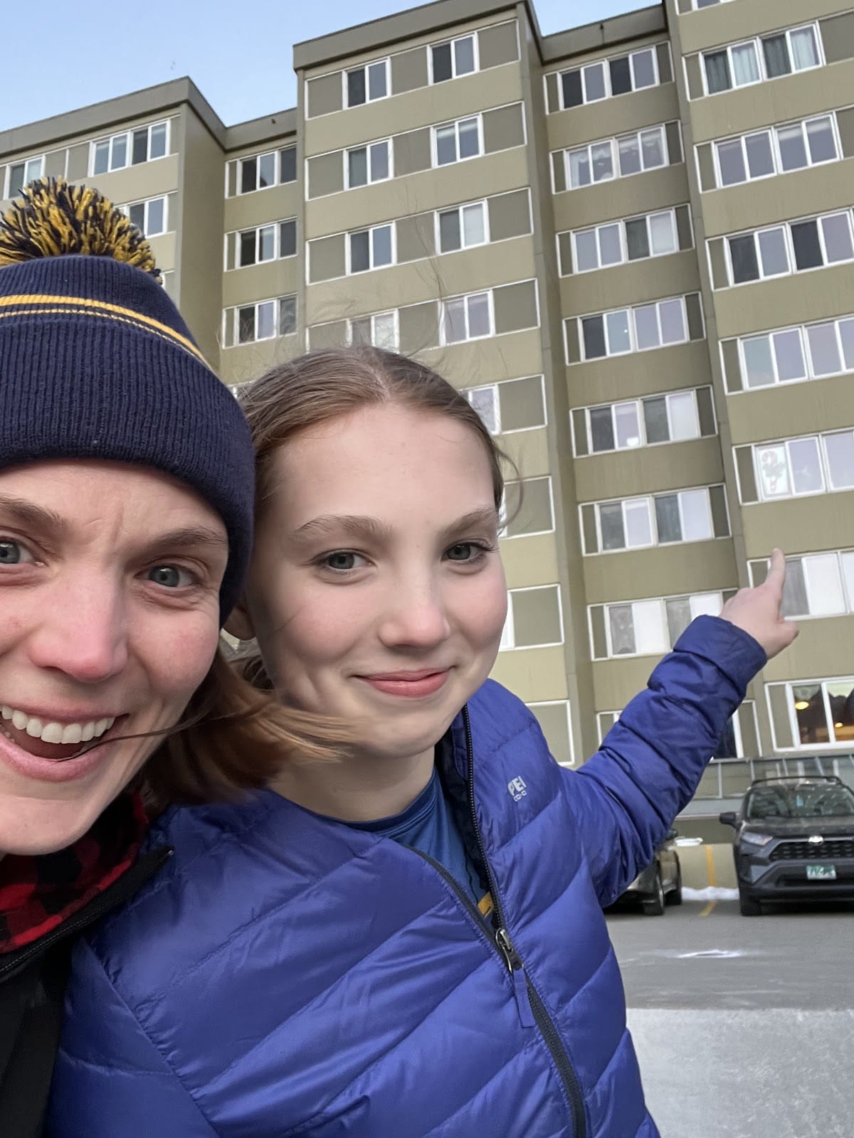 Selfie of a two people pointing to the building behind them.