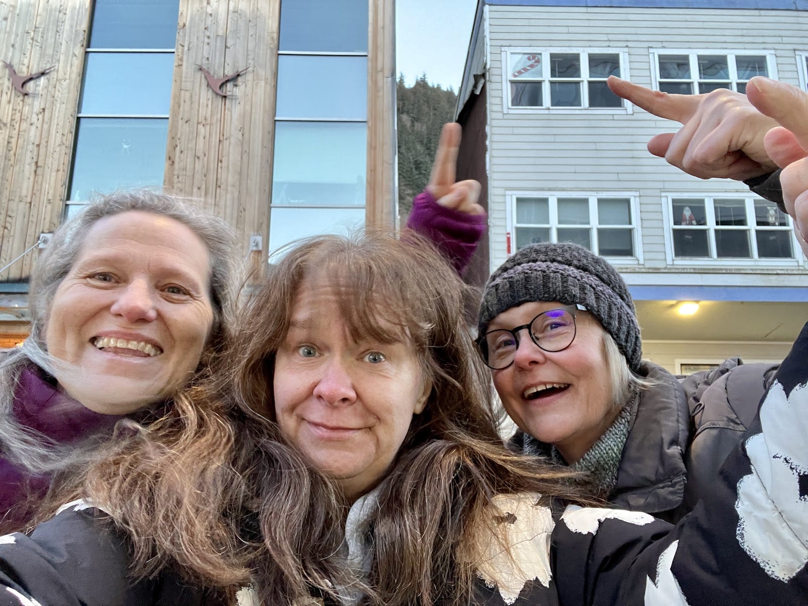 Selfie of three adults pointing to the window in the building behind them.