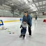 Photo of adult guiding young skater on ice