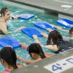 Photo of young swimmers practicing with kick boards as instructor watches