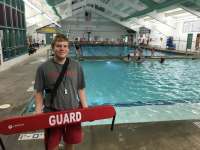 Photo of lifeguard standing in front of pool and holding red lifesaving device