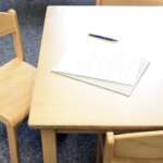 Photo of wooden table and chairs with paper and pen lying on the table