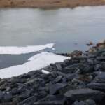 Photo of white foam floating in the water outside Mendenhall Wastewater Treatment Plant