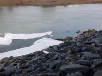 Photo of white foam floating in the water outside Mendenhall Wastewater Treatment Plant