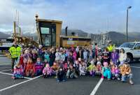 Photo of elementary students kneeling in front of CBJ grader with nameplate 