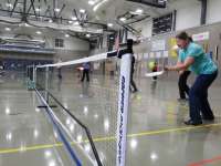 Photo of pickleball player in position behind net holding paddle and ball