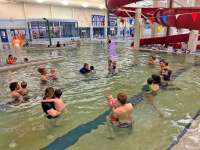 Several pairs of adults and very small children float in the pool during Parent & Tot swim lessons