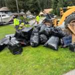 CBJ crews hauling a large pile of black trash bags full of flood debris away from a residential lawn