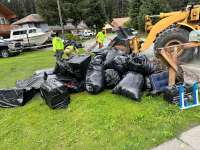 CBJ crews hauling a large pile of black trash bags full of flood debris away from a residential lawn