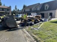 A clean-up crew approaches a driveway filled with piles of flood debris for removal