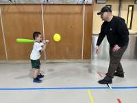 A young child swings a foam bat at a balloon as an adult watches