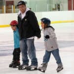 Adult skater holdings hands with two children on the rink ice