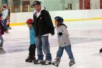 Adult skater holdings hands with two children on the rink ice