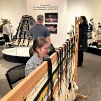 A weaver demonstrates Ravenstail weaving as museum visitors examine displays on the wall