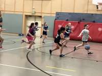 A group of small girls in basketball jerseys race down the court