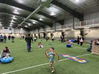 Young children play with hula hoops and other toys on the Field House turf as adults look on