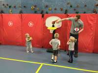 Three small children watch an adult show how the ball goes through a child-size basketball hoop