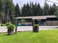 An image of a public park entrance featuring a wooden sign that reads 'Jackie Renninger Park.' Behind the sign, a skatepark building with the word 'Pipeline' displayed prominently on its facade is visible. The building is surrounded by lush green trees, creating a serene and inviting atmosphere.