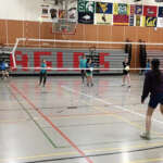 A young volleyball player prepares to receive serve from across the net.